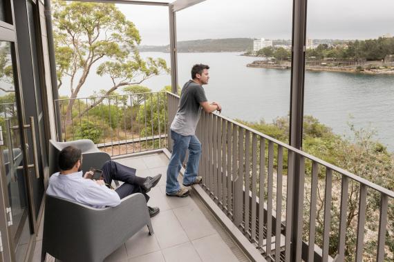 AIPM Venue - Two men on the deck. One sits in a chair whilst the other stands. Both looking out over the water.